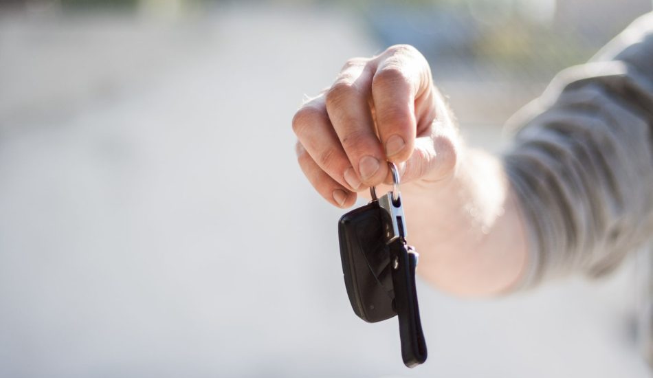 Hand holding out a set of car keys, ready to hand over to a used car buyer